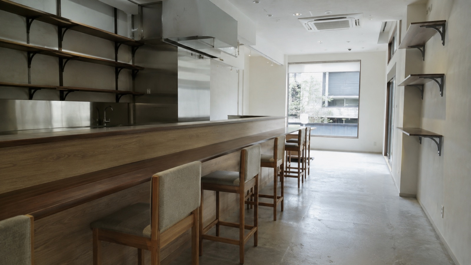 無人の店舗の客席側に残る造り付けのカウンターと椅子、壁面の棚