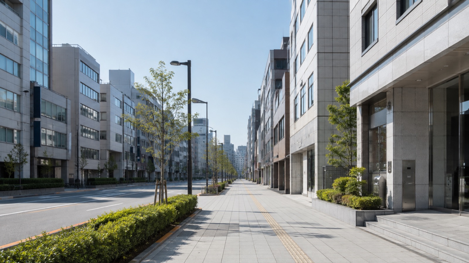 朝の光が差す東京の街路と中小規模のビルの並び